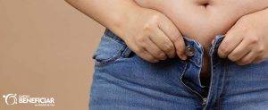Mulher tentando fechar uma calça jeans com a barriga inchada, consequência da retenção de líquido
