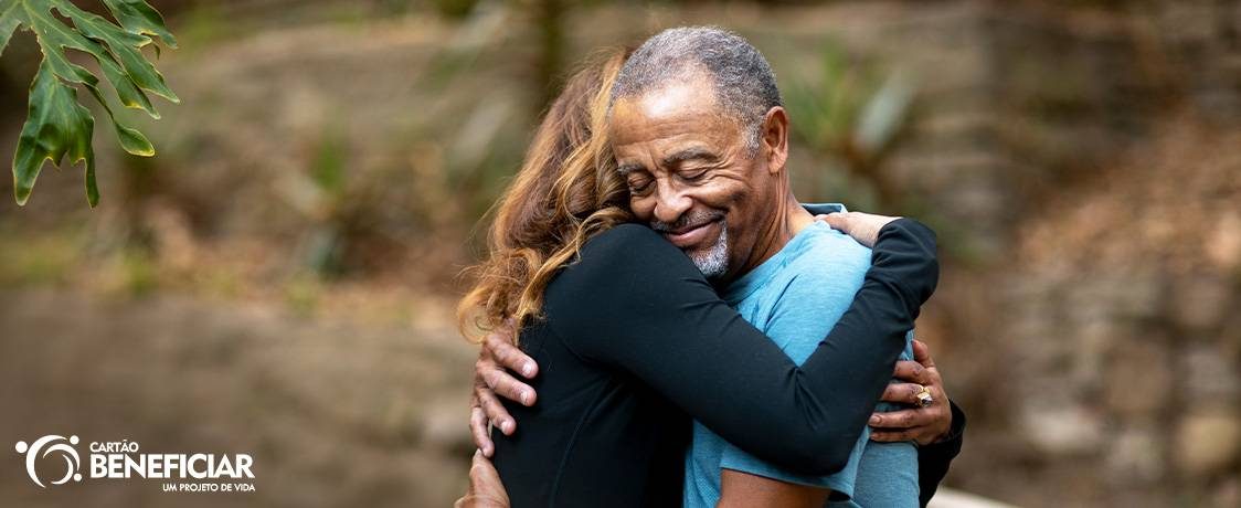Um homem negro usando roupa azul e uma mulher loira estão abraçados, mostrando que o apoio é uma das formas de ajudar alguém com crise de ansiedade